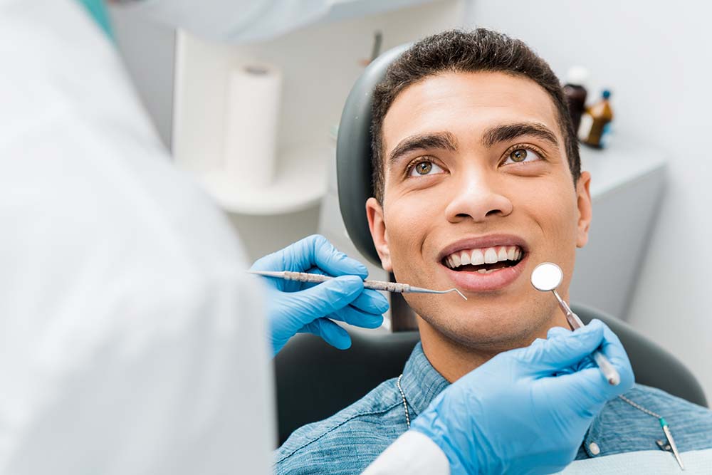 A man receiving dental treatment with a smile on his face while seated in a dentist s chair, surrounded by medical equipment and a dental professional in the background.