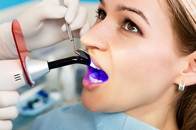 The image shows a person sitting in a dental chair with a purple device inserted into their mouth, receiving dental care from a professional wearing medical gloves and using dental tools.