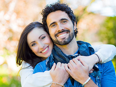 A young couple embracing each other outdoors with smiles on their faces.