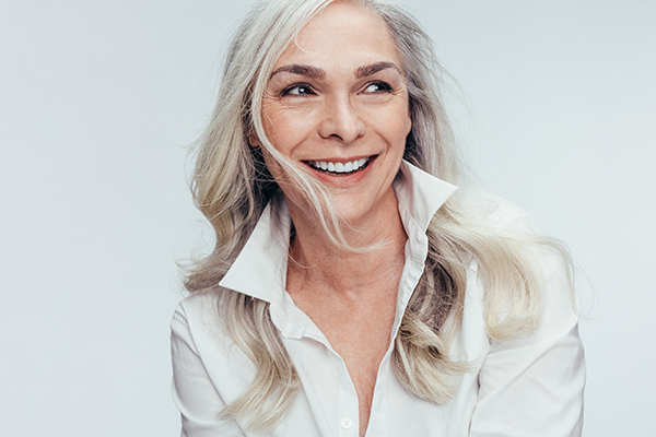 The image features a woman with blonde hair smiling at the camera while wearing a white shirt, posing against a light background.