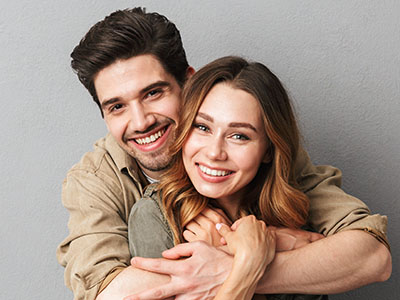 The image shows a man and woman hugging each other with smiles on their faces; they are both dressed casually, suggesting a relaxed, friendly atmosphere.