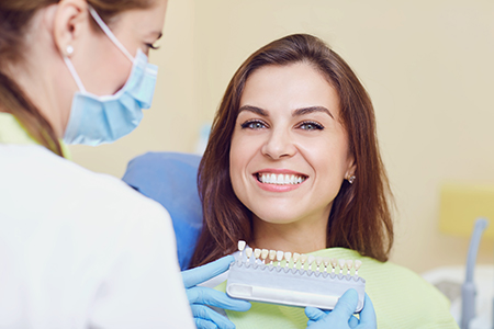 The image shows a woman sitting in front of a dental professional, receiving dental care with a smile on her face.