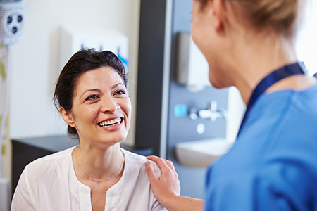 The image shows a woman with a smile, standing next to another person who appears to be a healthcare professional, possibly in a medical setting.