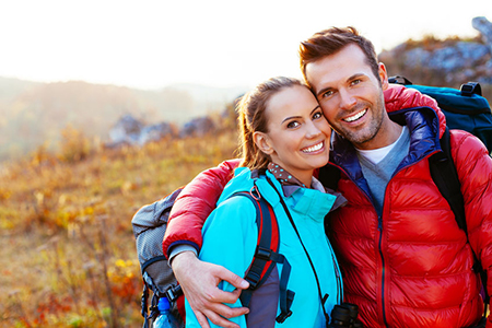 A man and woman posing together outdoors with backpacks, smiling at the camera.