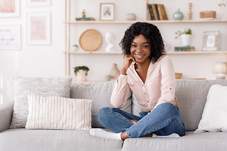 A young woman with curly hair sitting on a couch, smiling at the camera.