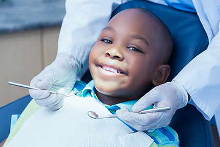 A young boy smiling while sitting in a dental chair with a dentist s hand holding his chin, receiving a dental treatment in a dental office setting.