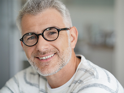 In the image, there are two photos of a man with glasses and facial hair, smiling at the camera. He appears to be in a good mood and is looking directly at the viewer.