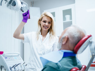 A female dental hygienist assisting an elderly patient with dental care equipment in a professional setting.