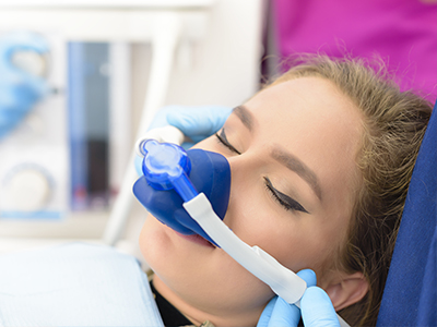 A woman lying down with a medical mask on her face, receiving oxygen therapy, while someone attends to her using medical equipment.