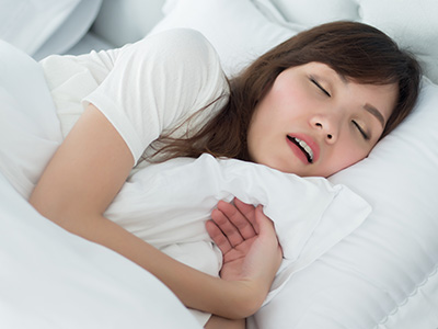 A woman sleeping peacefully on a bed with her eyes closed and mouth slightly open.